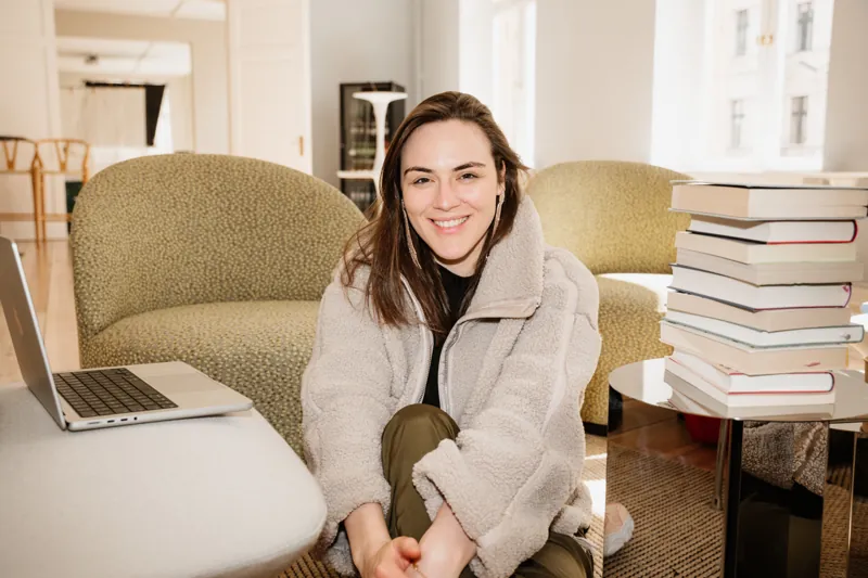 Victoria Weber sitzt lächelnd neben ihrem Laptop und einem Bücherstapel