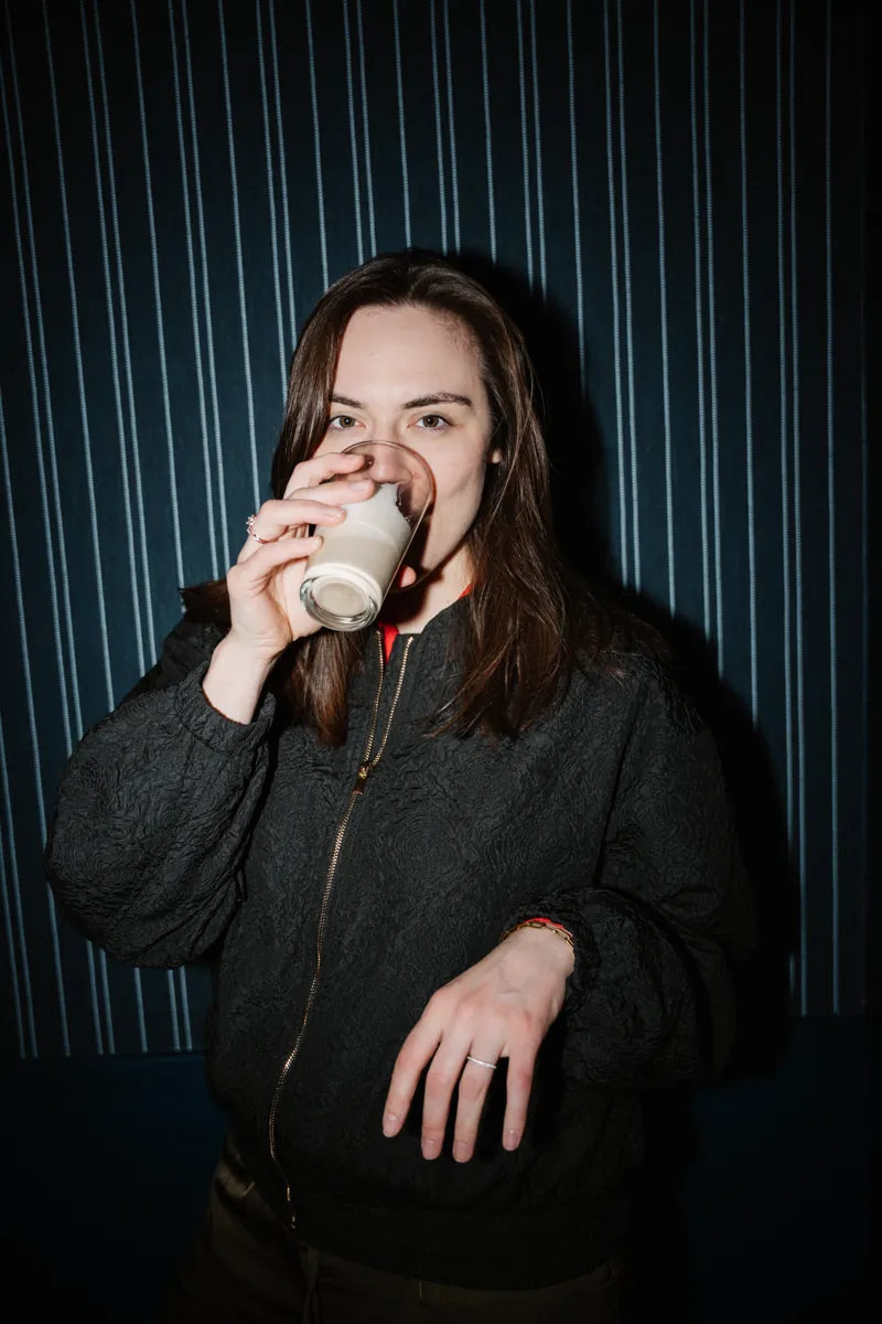 Porträt von Victoria Weber mit einem Glas in der Hand vor einer gestreiften Wand