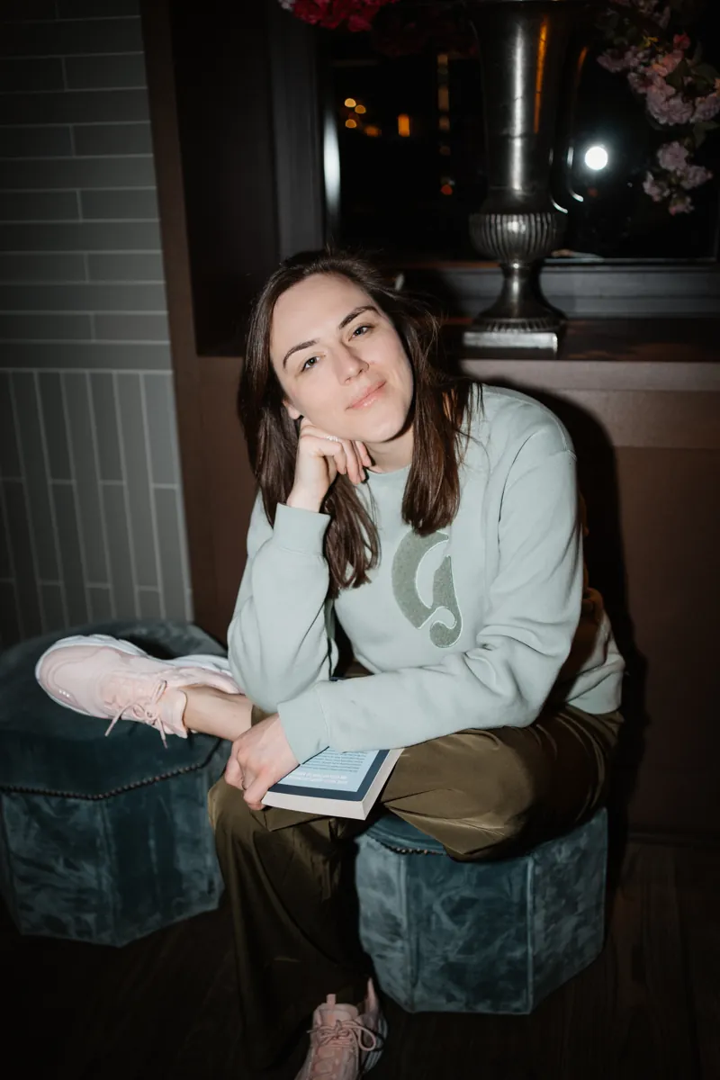 Victoria Weber, Gründerin von Creatorway, sitzt lächelnd mit einem Buch auf einem Hocker